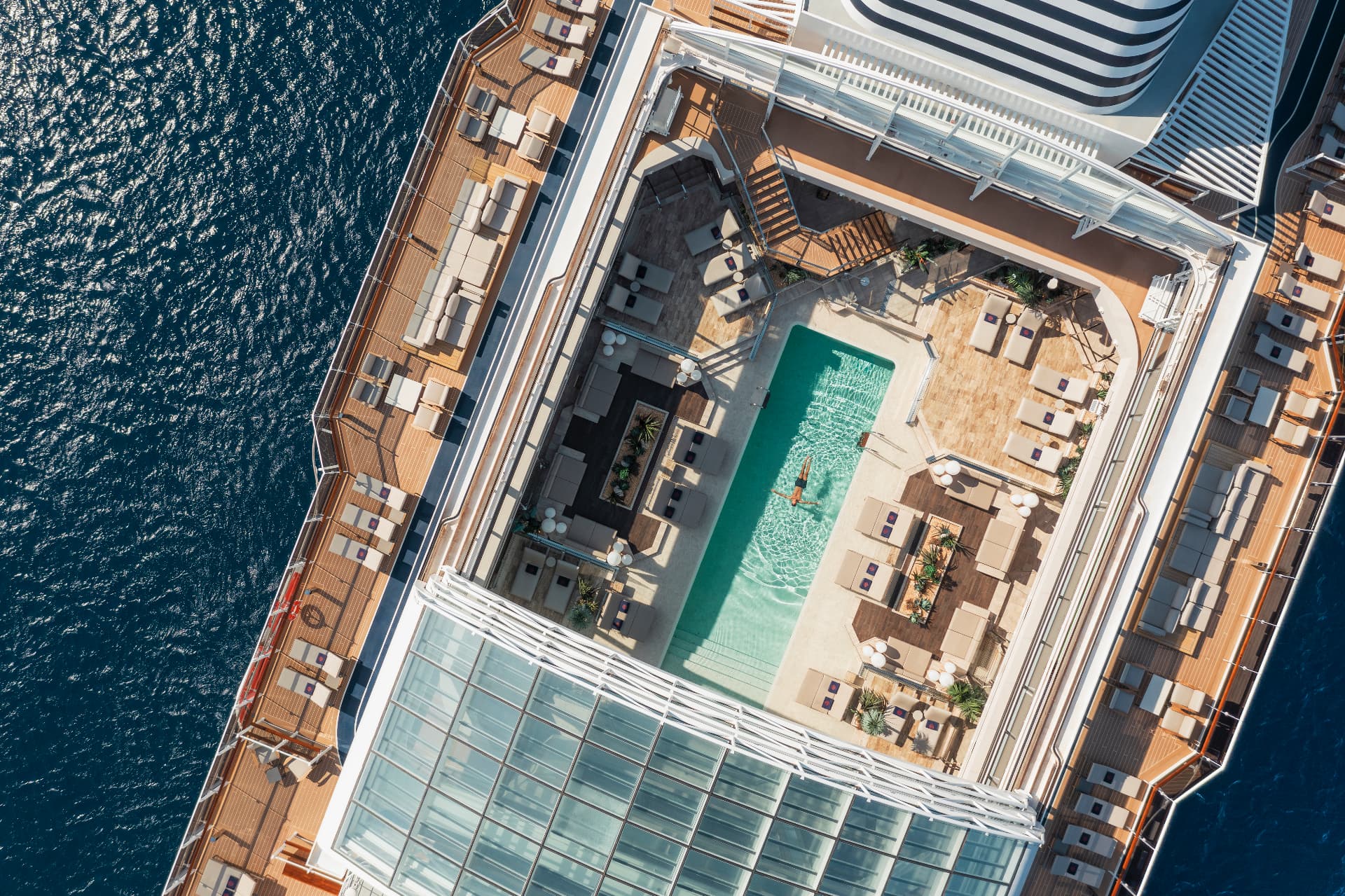Pont piscine d’un navire EXPLORA JOURNEYS vu du ciel, mer turquoise et transats
